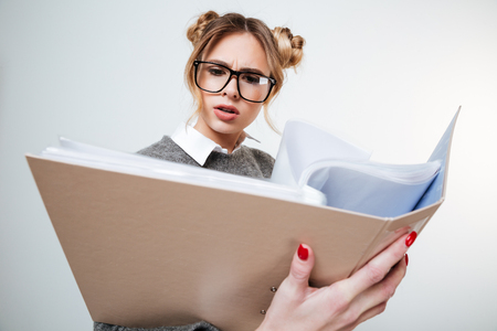 Serious frowning young woman in glasses reading documents in folderの写真素材