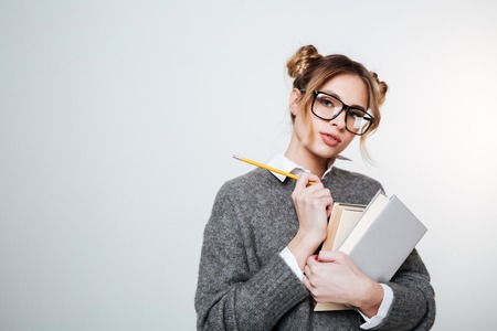 Pretty Woman in sweater and eyeglasses with books and pencil posing in studio and looking at camera. Isolated gray backgroundの写真素材