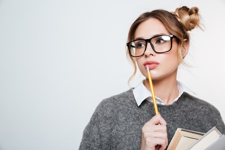 Close up portrait of woman in sweater and eyeglasses with books and pencil looking awayの写真素材