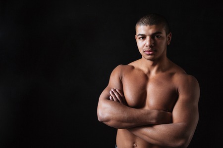 Image of handsome young african sportsman standing with arms crossed over black background and looking at camera.の写真素材