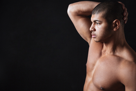 Image of serious young african sportsman posing over black background and looking aside.の写真素材