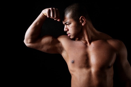 Handsome shirtless african american fitness man standing and showing biceps over black backgroundの写真素材