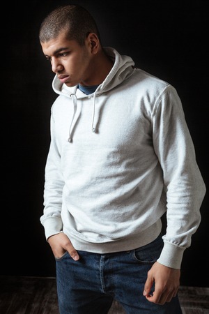 Thoughtful depressed african american young man in hoodie standing and thinking over black backgroundの写真素材