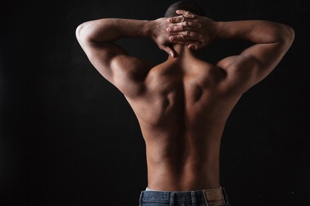 Back view picture of young african sportsman posing over black background.の写真素材