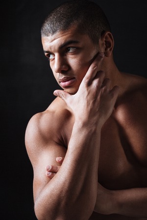 Portrait of attractive young african sportsman posing over black background and looking aside.の写真素材
