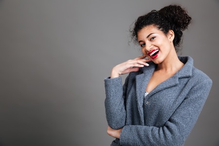 Portrait of a smiling young afro american woman wearing coat isolated on grey backgroundの写真素材
