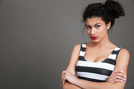 Irritated african american young woman standing with arms crossed over grey backgroundの写真素材