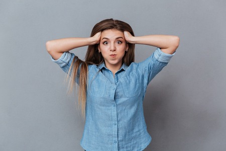 Funny Woman in shirt holding her head and looking at camera. Isolated gray background