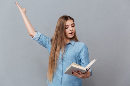 Concentrated woman in shirt rehearses in studio with book in hand. Isolated gray backgroundの写真素材