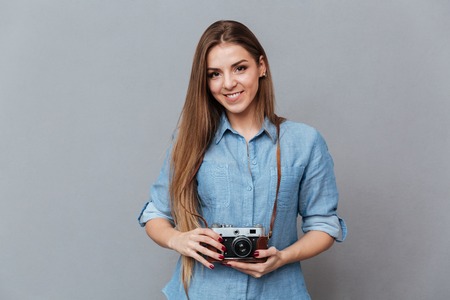 Woman in shirt holding retro camera in hands and looking at camera. Isolated gray backgroundの写真素材