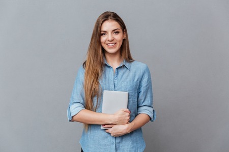 Woman in shirt holding book in hands and looking at camera. Isolated gray backgroundの写真素材