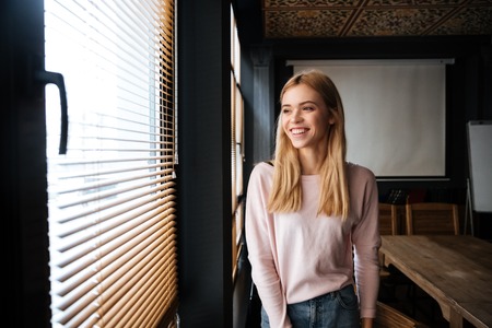 Image of attractive young cheerful woman standing in cafe and looking aside.の写真素材