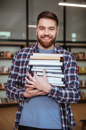 Portrait of a smiling cheerful man student holding books in libraryの写真素材