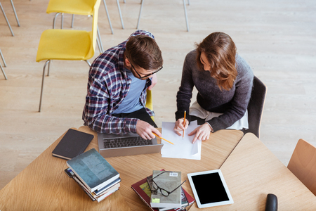 Image of young concentrated students sitting in library while writing notes.の写真素材