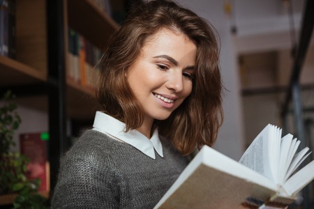 Close up of a smiling student girl reading book in libraryの写真素材
