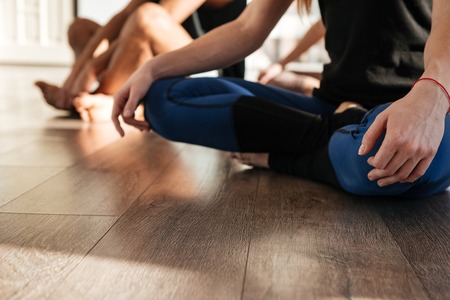 Closeup of woman sitting with legs crossed and practicing yoga in group at studioの写真素材