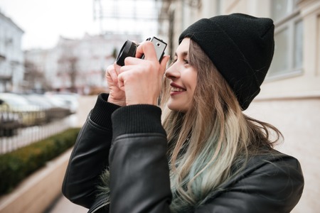 Image of young cheerful woman wearing hat walking on the street while holding camera.の写真素材