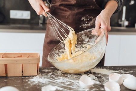 Cropped photo of young woman standing in kitchen and cooking the dough.