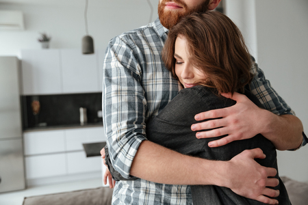 Cropped image of young loving couple hugging in kitchen at home indoors. Eyes closed.の写真素材