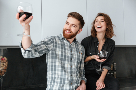 Photo of young smiling loving couple standing in kitchen at home indoors. Drinking alcohol.の写真素材