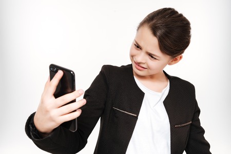 Photo of attractive young girl standing and holding phone isolated over white background.の写真素材