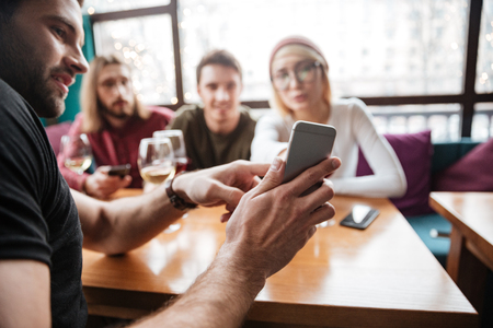 Photo of attractive friends sitting in cafe and drinking alcohol and looking at phone.の写真素材