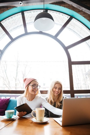 Two happy pretty young women using laptop and tablet in cafeの写真素材