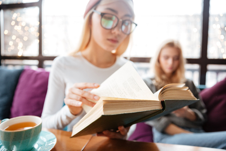 Closeup of two attractive young women sitting and reading books in cafeの写真素材