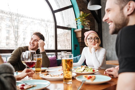 Image of attractive happy friends sitting in cafe eating and drinking alcohol.の写真素材