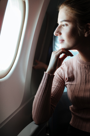 Vertical image of pensive woman which looking in porthole of aircraftの写真素材