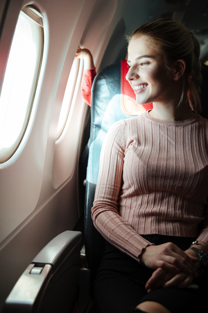 Vertical image of Happy woman which sitting in aircraft and looking at portholeの写真素材