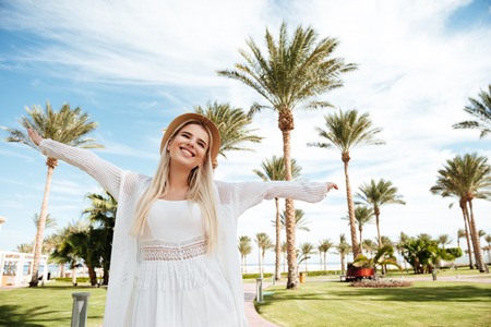 Cheerful carefree young woman in hat standing and having fun on summer resortの写真素材