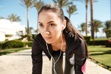 Closeup of pretty young woman athlete with earphones ready to run in summerの写真素材