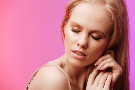 Picture of young attractive woman standing and posing over pink background. Eyes closed.の写真素材