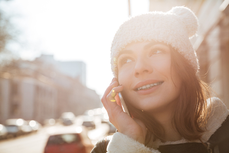 Image of amazing young woman walking on the street wearing hat while talking by phone.の写真素材