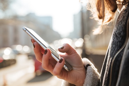 Cropped picture of young attractive woman walking on the street while using mobile phone.