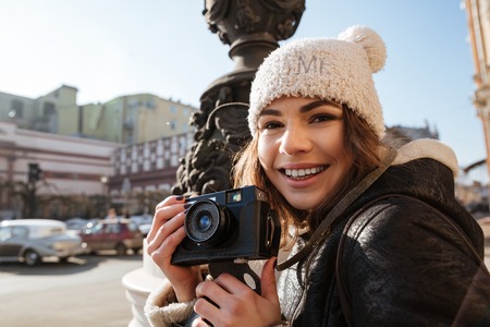 Image of pretty young woman walking on the street wearing hat while holding camera.の写真素材