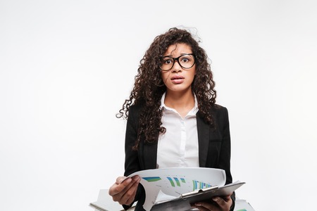 Photo of shocked african business lady wearing glasses reading gazette over white background. Looking at camera.の写真素材
