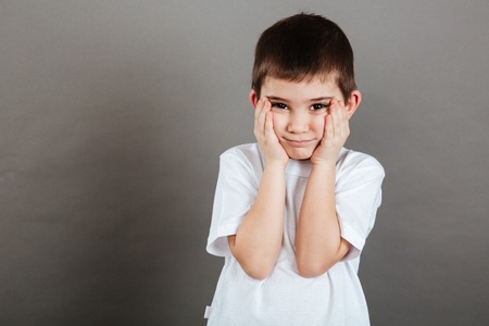 Sad cute little boy standing with hands on cheeksの写真素材