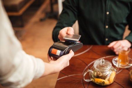 Cropped image of amazing young man sitting in cafe. Pays the order with mobile phone.の写真素材
