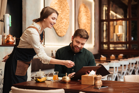 Photo of smiling bearded young man sitting in cafe. Looking at menu list.の写真素材