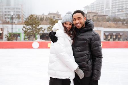 Photo of young cheerful loving couple skating at ice rink outdoors. Looking at camera.の写真素材