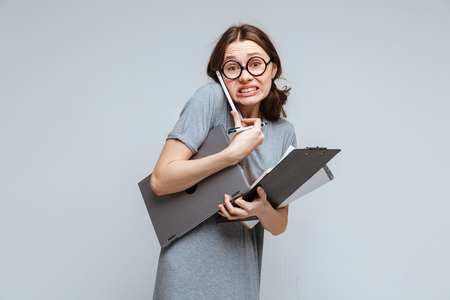 Guilty female nerd in funny eyeglsses which talking on phone and holding laptop, clipboard and notebookの写真素材