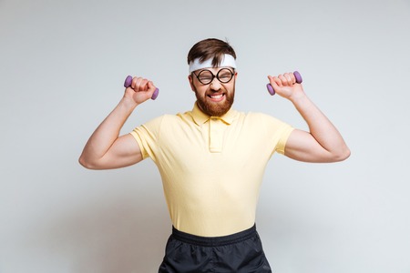 Male nerd in funny glasses and yellow shirt which training with light dumbbellsの写真素材