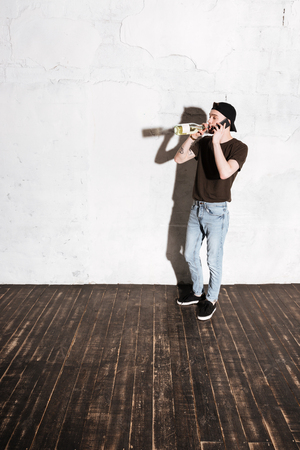 Vertical image of Hipster in snap back drinking wine and talking on phoneの写真素材