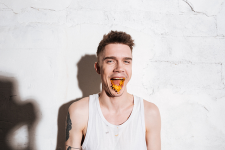 Cheerful young man eating potato chips and having fun over white backgroundの写真素材
