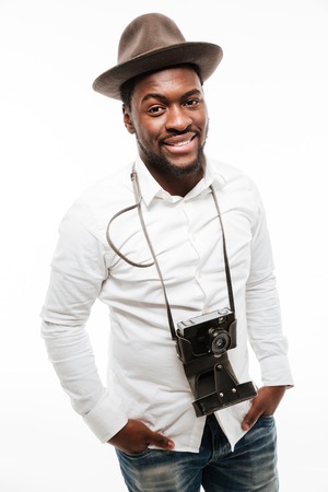 Picture of happy young african man dressed in shirt wearing hat standing with camera isolated over...