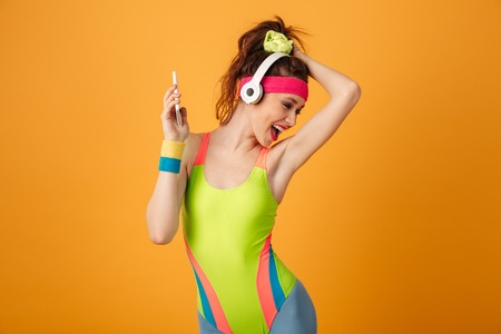 Happy young woman athlete listening to music from smartphone and dancing over yellow backgroundの写真素材