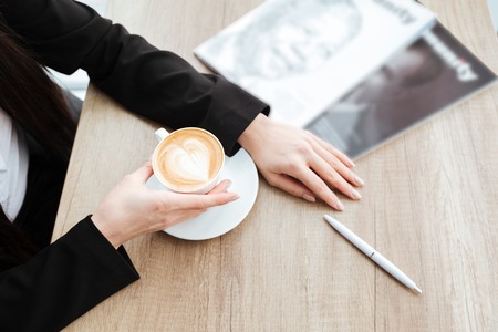 Top view of businesswoman sitting at the table and drinking coffee with milkの写真素材