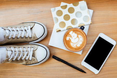 Top view of wooden board with phone, cofee, pen, gumshoes and notebookの写真素材